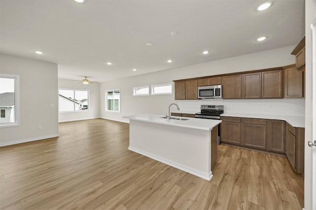 kitchen with an island with sink, sink, light wood-type flooring, appliances with stainless steel finishes, and ceiling fan