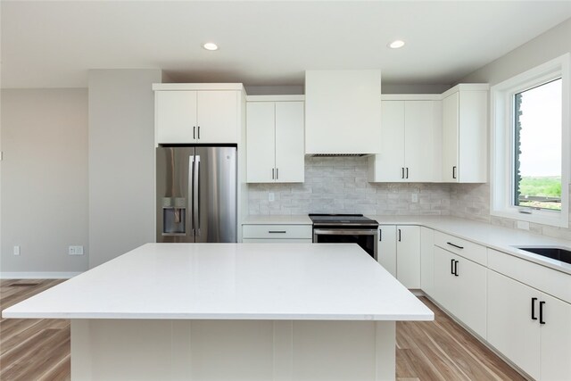 kitchen featuring appliances with stainless steel finishes, a kitchen island, tasteful backsplash, white cabinets, and light wood-type flooring