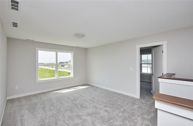 empty room featuring carpet floors, a wealth of natural light, visible vents, and baseboards