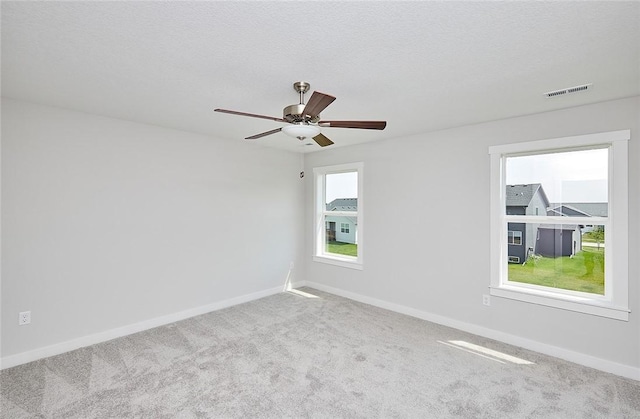 empty room with a textured ceiling, carpet floors, visible vents, and baseboards