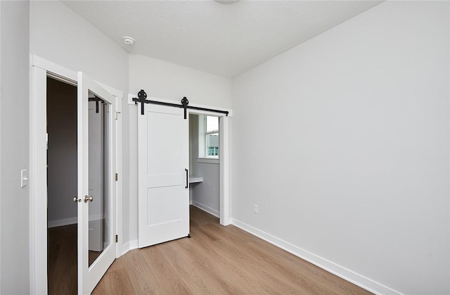 unfurnished bedroom with light wood-style flooring, baseboards, and a barn door