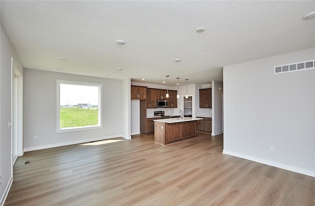 kitchen featuring visible vents, an island with sink, appliances with stainless steel finishes, open floor plan, and light countertops