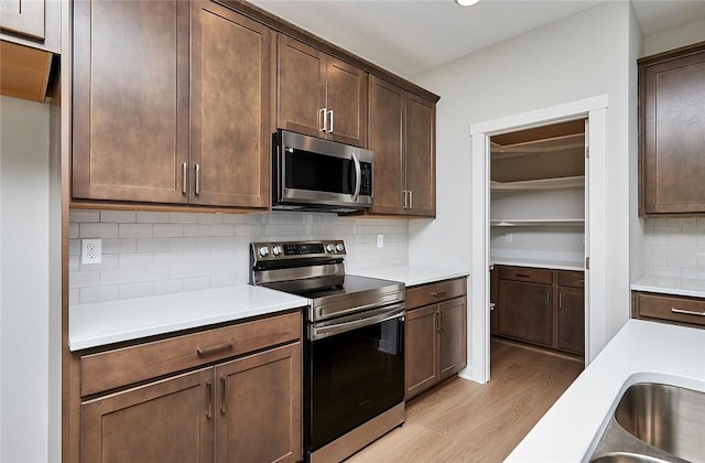 kitchen featuring light countertops, appliances with stainless steel finishes, light wood-type flooring, and tasteful backsplash