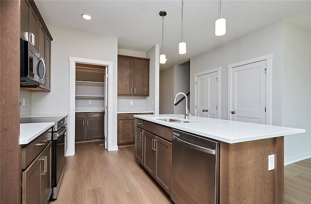 kitchen featuring hanging light fixtures, tasteful backsplash, light hardwood / wood-style flooring, a kitchen island with sink, and appliances with stainless steel finishes