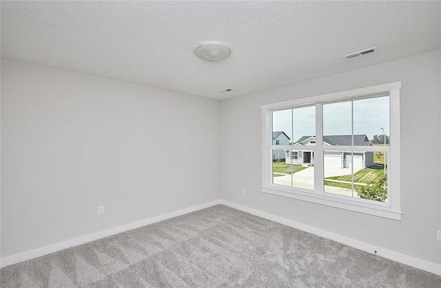 carpeted empty room featuring a textured ceiling, visible vents, and baseboards