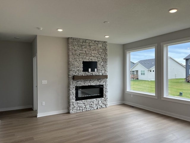 unfurnished living room with a healthy amount of sunlight, baseboards, wood finished floors, and a stone fireplace