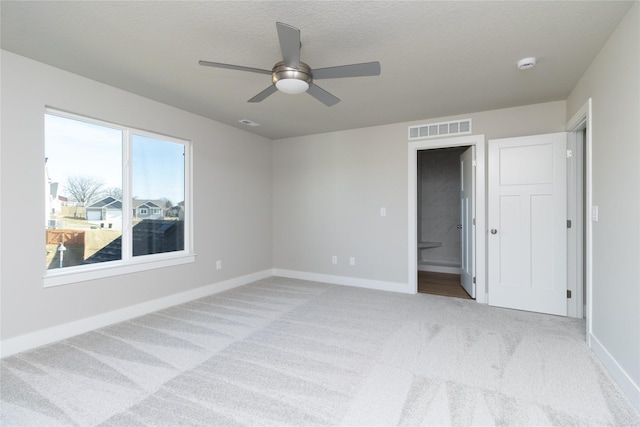 unfurnished bedroom with ceiling fan, connected bathroom, light carpet, and a textured ceiling