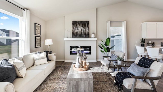 living area with vaulted ceiling, a glass covered fireplace, dark wood finished floors, and baseboards