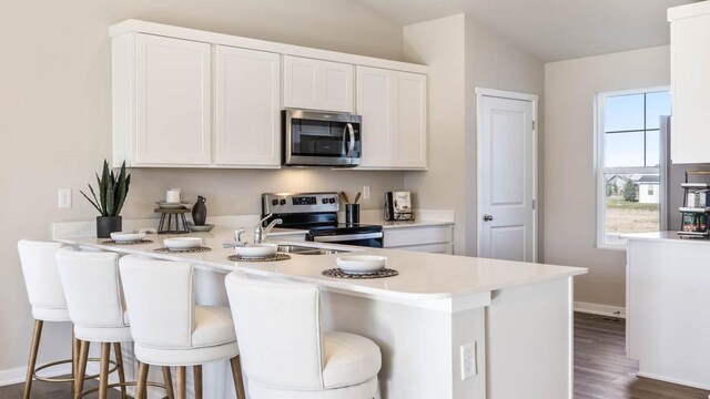 kitchen featuring lofted ceiling, kitchen peninsula, white cabinetry, stainless steel appliances, and a kitchen breakfast bar