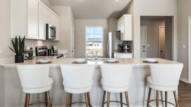 kitchen with dark wood-type flooring, white cabinets, kitchen peninsula, a kitchen bar, and stainless steel appliances