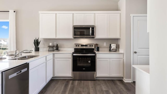 kitchen with stainless steel appliances, a sink, white cabinets, light countertops, and dark wood finished floors