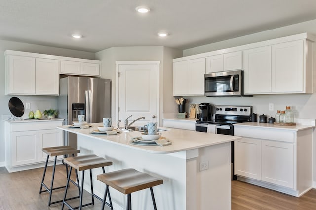 kitchen with white cabinets, an island with sink, appliances with stainless steel finishes, and light hardwood / wood-style flooring