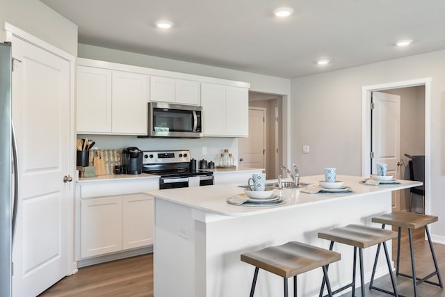 kitchen featuring white cabinets, a center island with sink, hardwood / wood-style flooring, appliances with stainless steel finishes, and a breakfast bar area