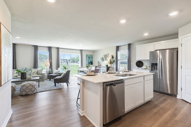 kitchen with appliances with stainless steel finishes, a center island with sink, white cabinetry, and dark wood-type flooring