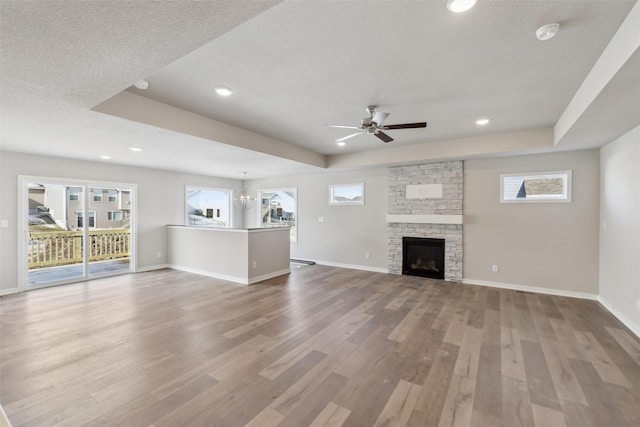 unfurnished living room featuring ceiling fan with notable chandelier, a raised ceiling, a fireplace, and hardwood / wood-style flooring