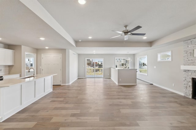 unfurnished living room featuring a ceiling fan, a sink, a stone fireplace, light wood-type flooring, and baseboards