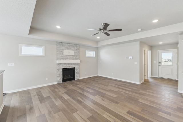 unfurnished living room featuring light wood-type flooring, a raised ceiling, ceiling fan, and a stone fireplace