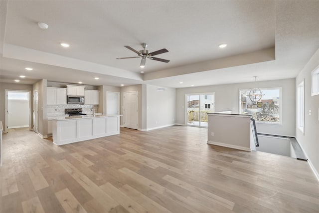 unfurnished living room with ceiling fan with notable chandelier, light hardwood / wood-style floors, and a tray ceiling