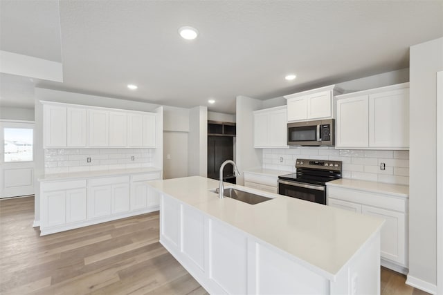 kitchen with sink, white cabinetry, light wood-type flooring, electric stove, and a kitchen island with sink