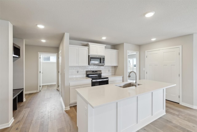 kitchen with sink, stainless steel appliances, white cabinetry, and a kitchen island with sink