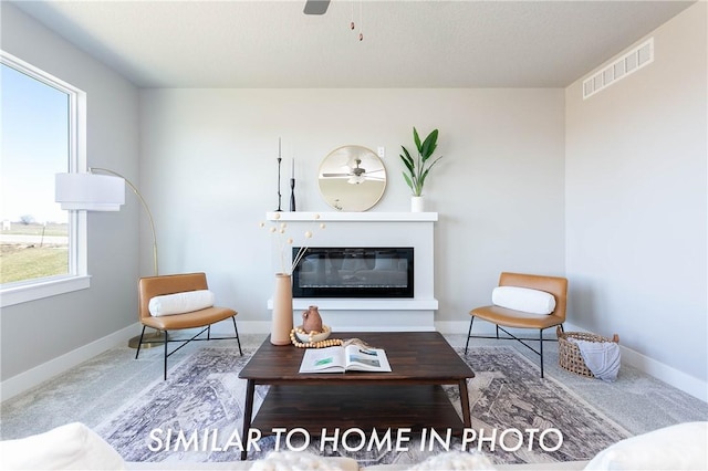 living area featuring a glass covered fireplace, visible vents, ceiling fan, and baseboards