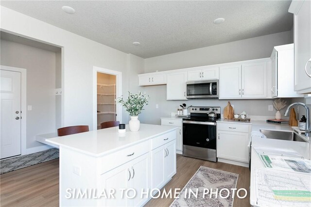 kitchen featuring a kitchen island, appliances with stainless steel finishes, sink, white cabinetry, and light wood-type flooring