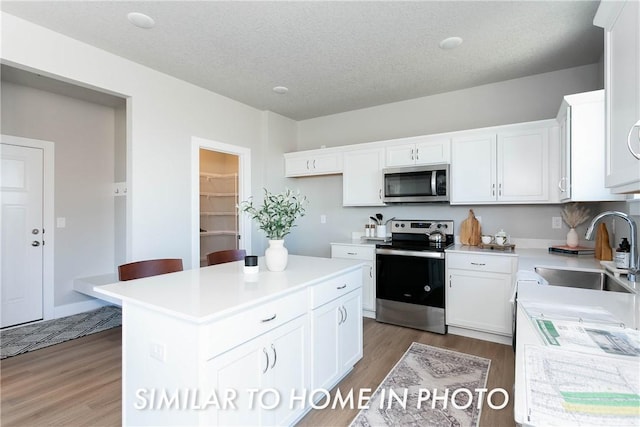 kitchen with a center island, light countertops, appliances with stainless steel finishes, white cabinetry, and a sink