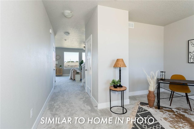 hallway with light carpet, baseboards, visible vents, and a textured ceiling