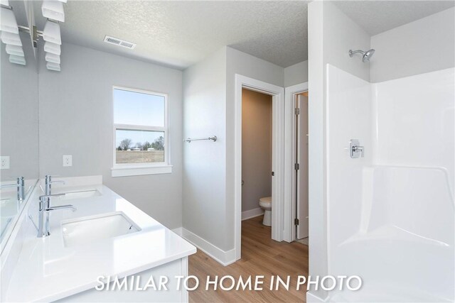 bathroom with a textured ceiling, vanity, hardwood / wood-style floors, walk in shower, and toilet