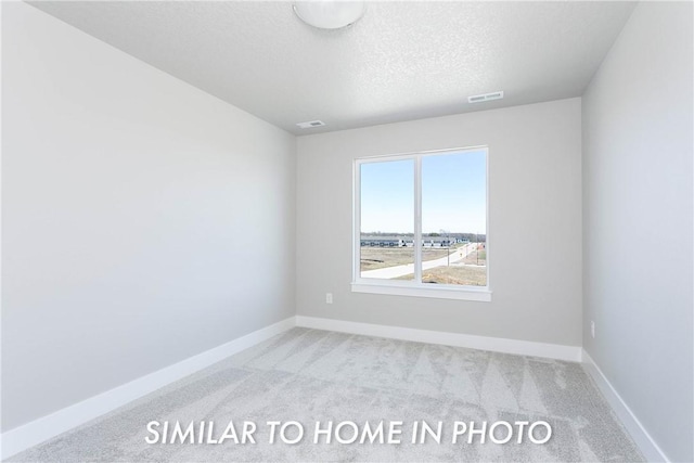 spare room with light carpet, a textured ceiling, visible vents, and baseboards