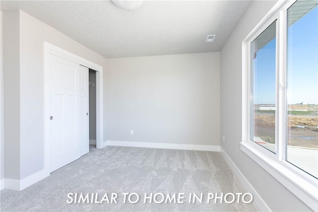 unfurnished bedroom with a closet, visible vents, light colored carpet, a textured ceiling, and baseboards