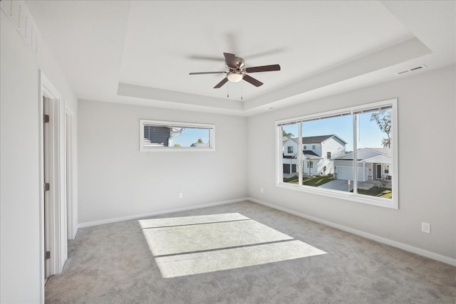 empty room with ceiling fan, light colored carpet, and a tray ceiling