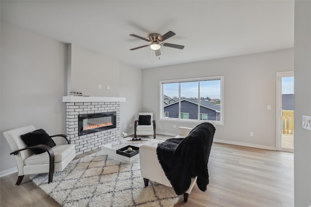 living room featuring ceiling fan, light wood-type flooring, and a brick fireplace