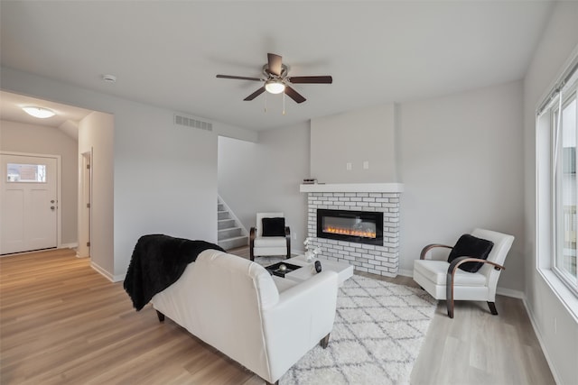 living room featuring ceiling fan, plenty of natural light, light hardwood / wood-style floors, and a brick fireplace