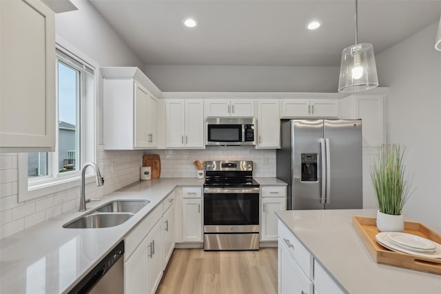 kitchen with stainless steel appliances, a sink, white cabinetry, light countertops, and light wood finished floors