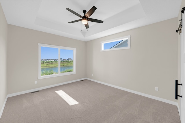 carpeted spare room featuring ceiling fan, a water view, and a tray ceiling