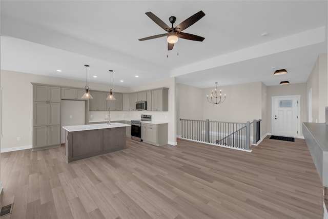 kitchen featuring appliances with stainless steel finishes, a center island with sink, decorative light fixtures, and gray cabinetry