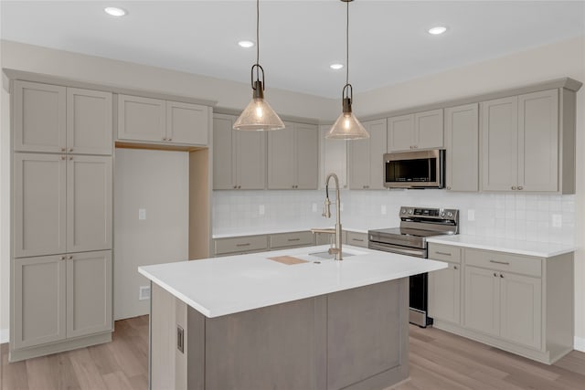 kitchen with hanging light fixtures, sink, an island with sink, and stainless steel appliances