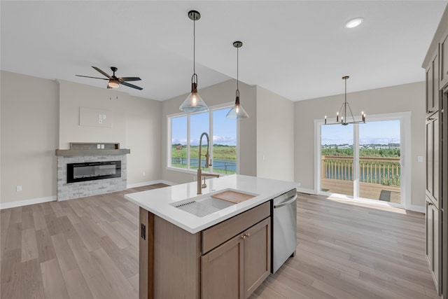 kitchen featuring dishwasher, sink, a fireplace, ceiling fan with notable chandelier, and a center island with sink