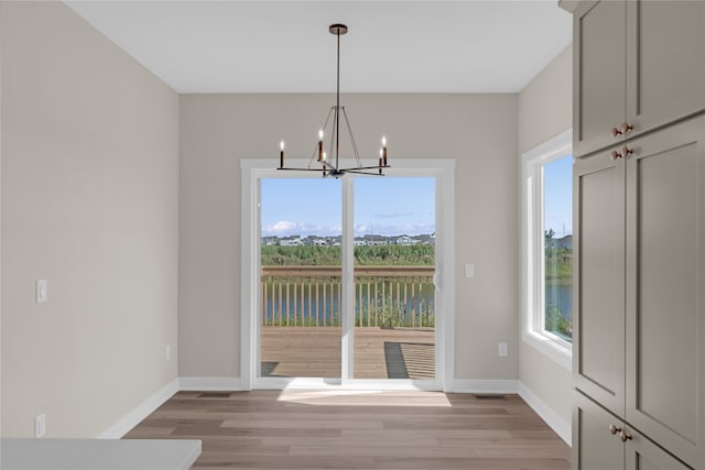 unfurnished dining area with a water view, an inviting chandelier, and light hardwood / wood-style floors