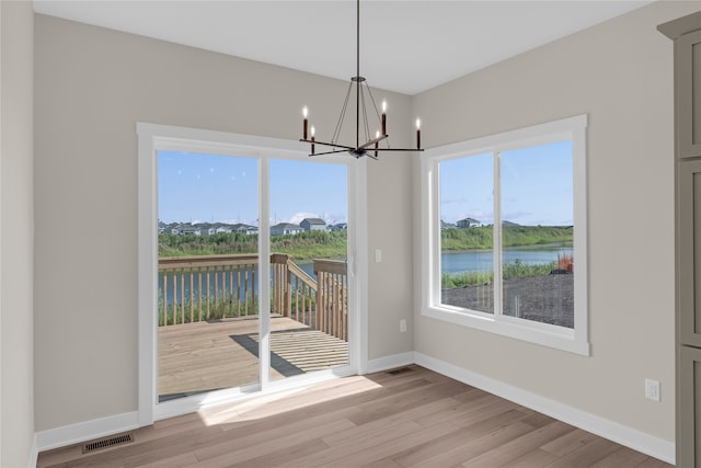 unfurnished dining area featuring light wood-type flooring, a water view, and a notable chandelier