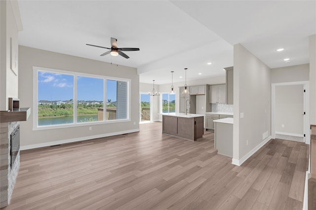 unfurnished living room with light wood-type flooring, ceiling fan with notable chandelier, a water view, and sink