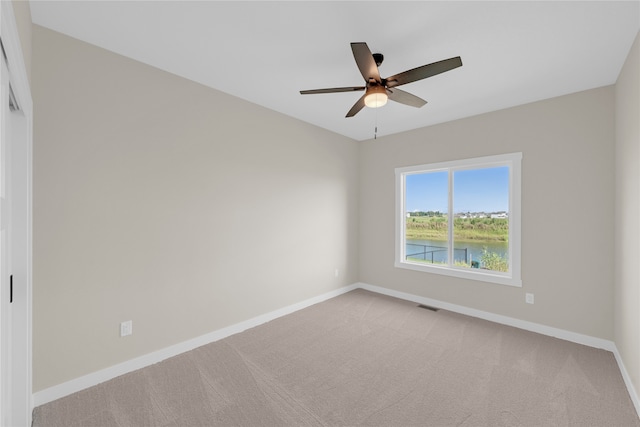 carpeted spare room with ceiling fan and a water view