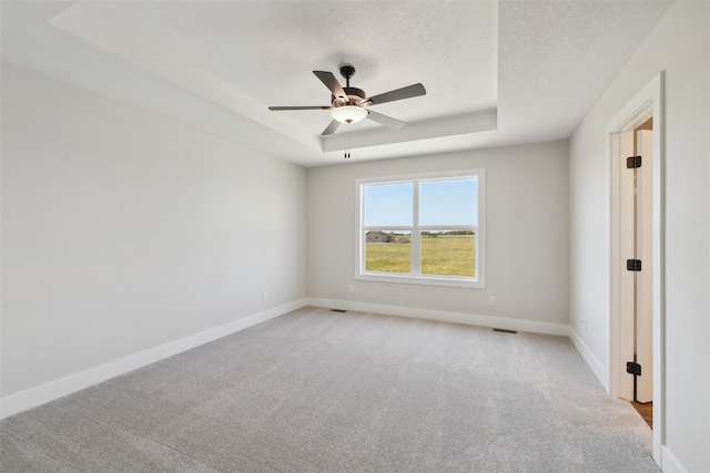 unfurnished room with ceiling fan, light colored carpet, a textured ceiling, and a raised ceiling