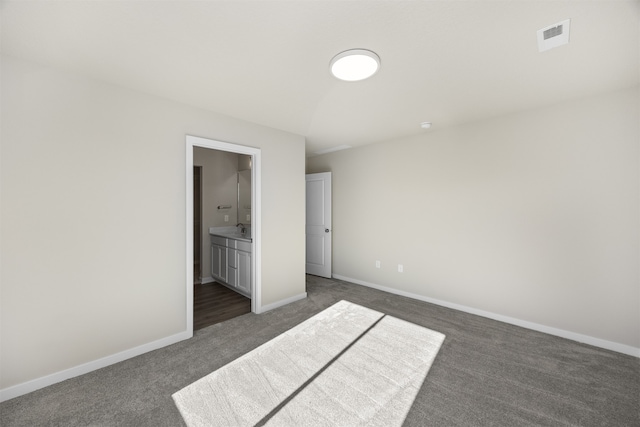 unfurnished bedroom featuring dark carpet and ensuite bath