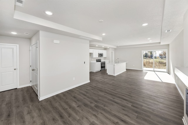 unfurnished living room featuring dark wood-type flooring, a textured ceiling, sink, and a raised ceiling