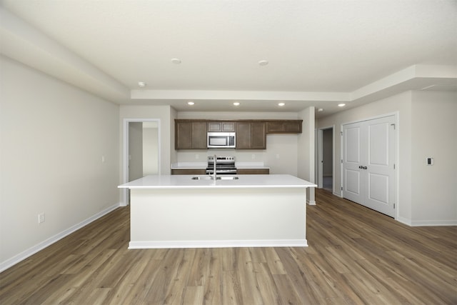 kitchen with dark brown cabinetry, dark hardwood / wood-style floors, a center island with sink, and appliances with stainless steel finishes