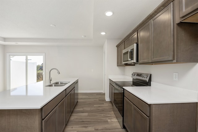 kitchen with stainless steel appliances, light hardwood / wood-style floors, dark brown cabinetry, a center island with sink, and sink