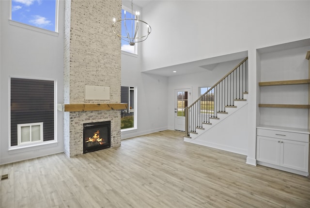 unfurnished living room with a fireplace, a towering ceiling, an inviting chandelier, and light hardwood / wood-style flooring