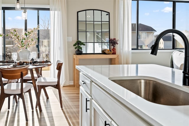 kitchen featuring a wealth of natural light, white cabinets, sink, and hanging light fixtures